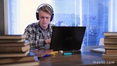英俊的学生用耳机和笔记本电脑<strong>在线学习</strong>，他正在做笔记练习册在桌子上